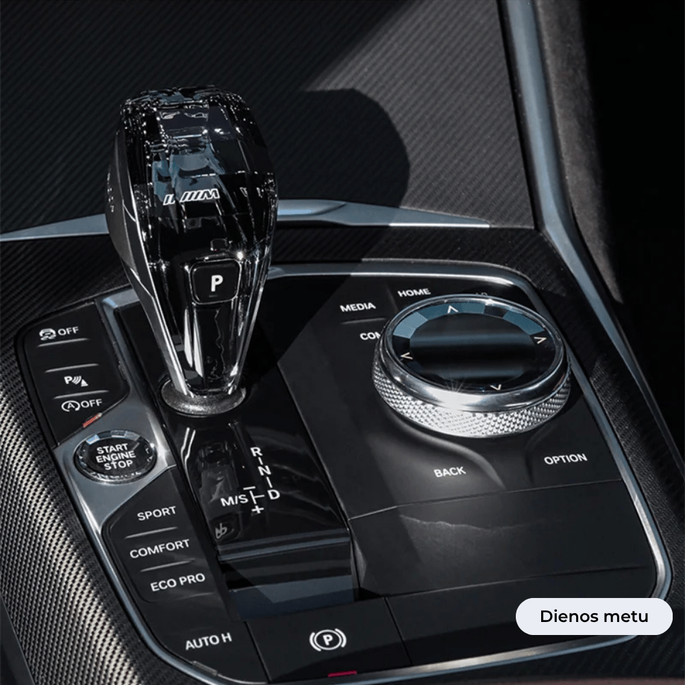 BMW automobilio interjeras su Crystal pavarų perjugimo svirtimi, sukamuoju valdymo ratuku ir įvairiais važiavimo režimo mygtukais vaizdas dieną.